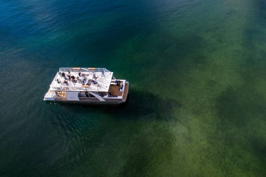 Party pontoon boat on lake – Hayden Lake An aerial view of a large, pleasant lake. A pontoon boat with an upper deck has many passengers having fun.