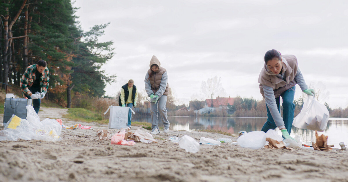 atxpartyboats-363084-cleaning-lake-trash-blogbanner1 A group of young people walking along the beach by a lake. They're carrying bags and working to clean up trash.