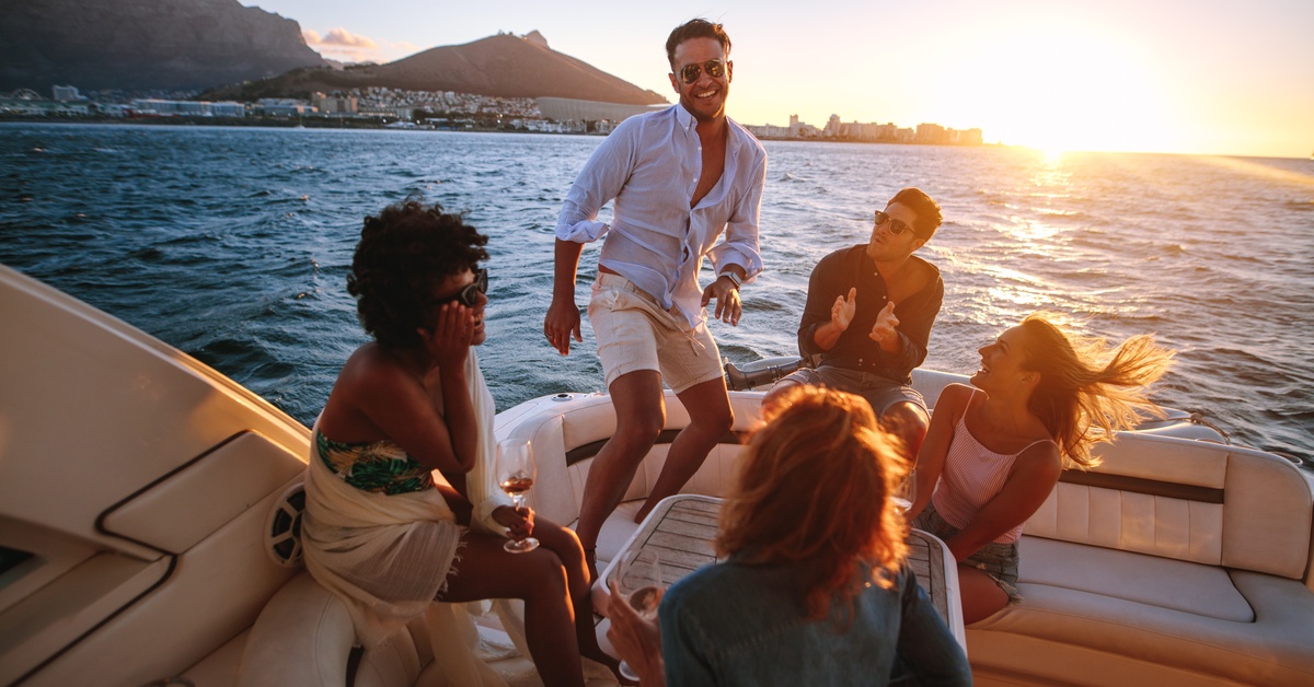 Your Guide to Choosing the Perfect Boat for Your Group Size A group of young people in a circle on the deck of a party boat. Some are sitting, while a young man is standing and dancing.