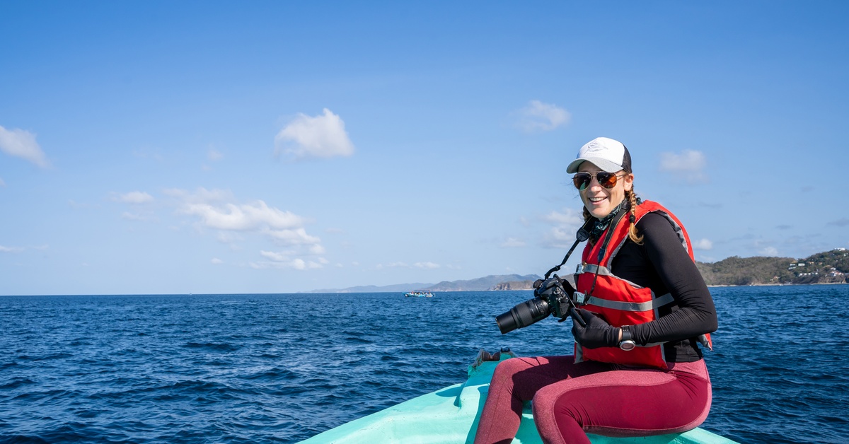A woman in a wetsuit and life vest is sitting on the edge of a boat, She’s holding a high-tech digital camera. A woman in a wetsuit and life vest is sitting on the edge of a boat, She's holding a high-tech digital camera.