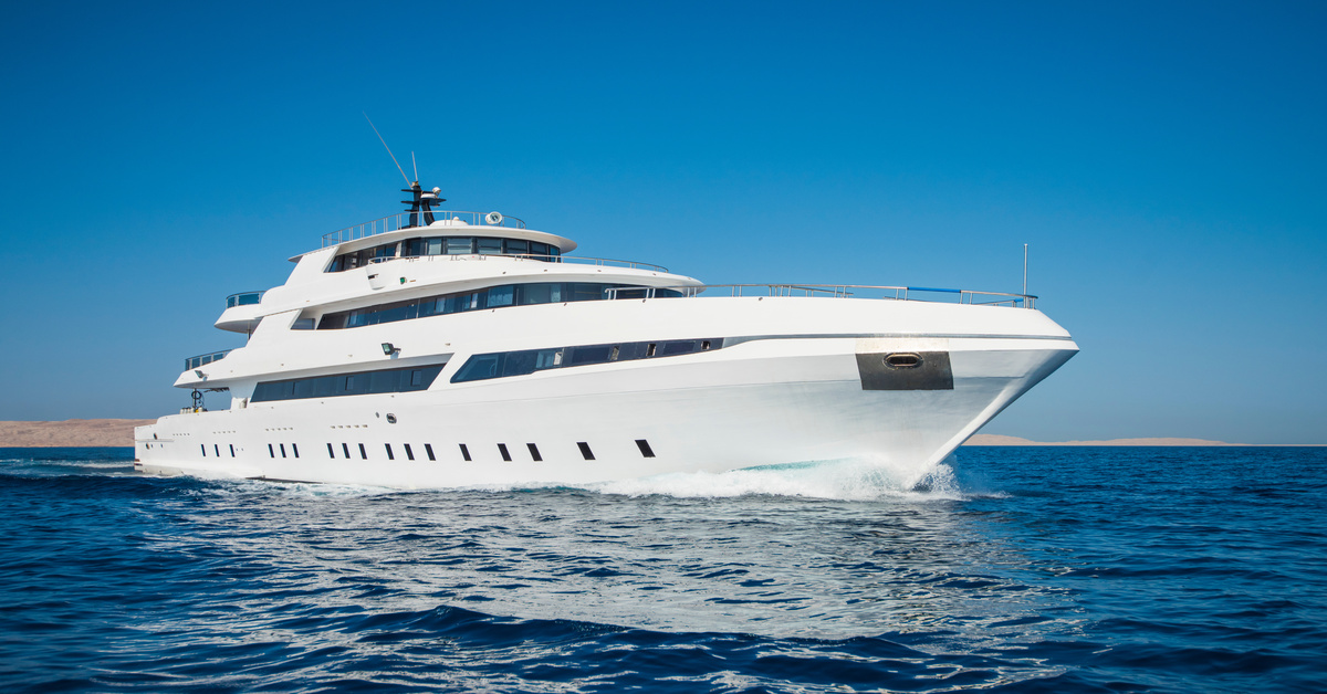 A large, white, multilevel yacht is sailing on dark blue waters. The clear blue sky stretches out behind it.