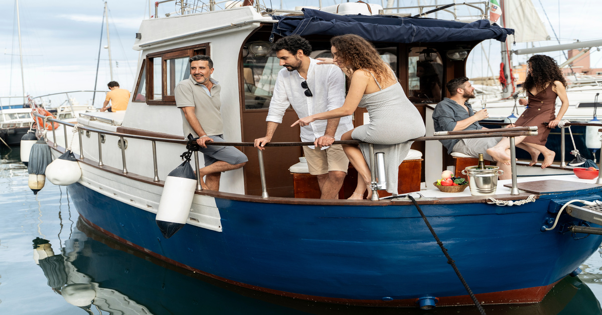 A group of friends hanging out on the stern of a blue and white classic motorboat in a marina on a sunny day.
