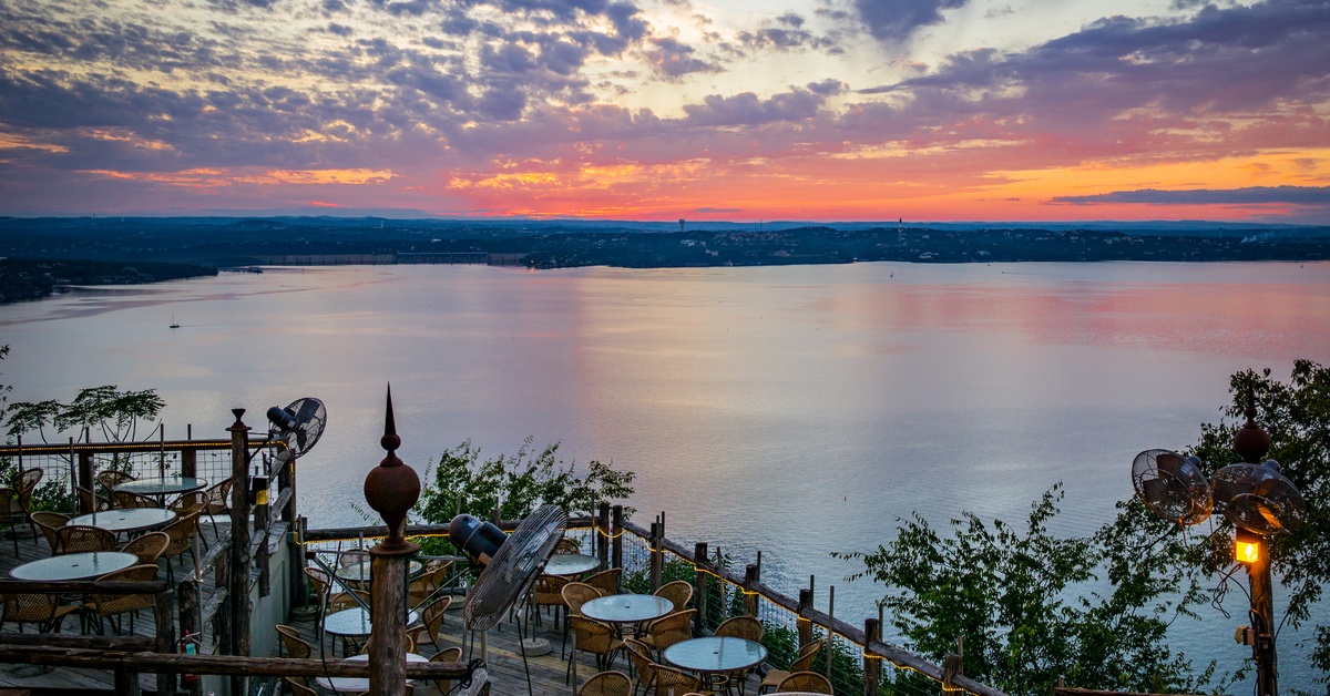 A panoramic view of Lake Travis from above on a large patio overlooking the lake as the sun sets over the horizon.