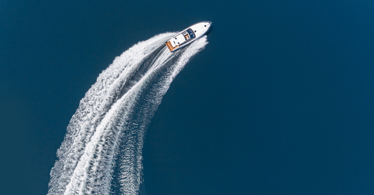 An aerial, drone view of a white speedboat turning at high speed on a blue lake, causing a long wake behind it.